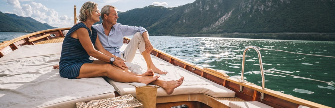 Man and woman sit in a boat looking out at the water and mountainside in the distance